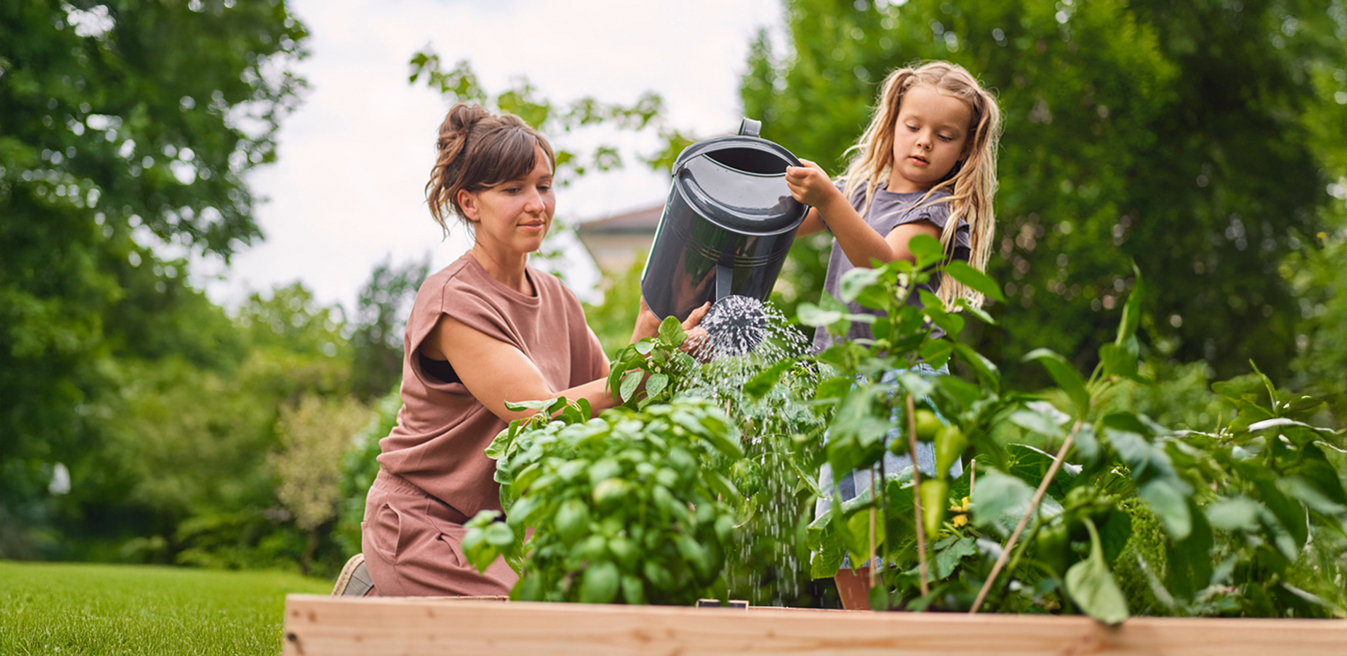 Mutter und Kind gießen das Hochbeet mit einer Gießkanne.