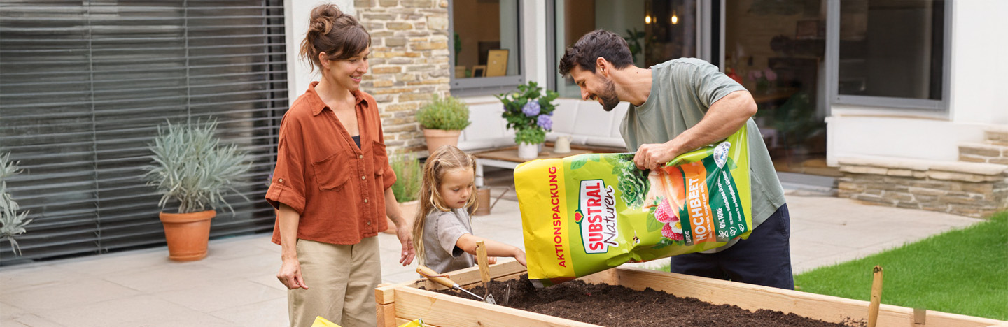 Mutter, Tochter und Vater befüllen ihr Hochbeet mit unserer Substral® Naturen® Hochbeeterde Torffrei.
