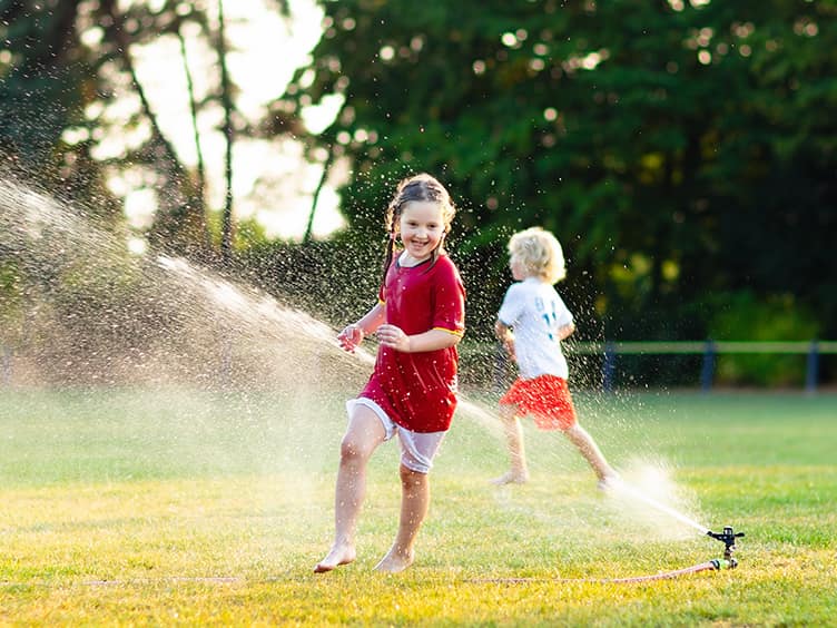 Two children running under a sprinkler