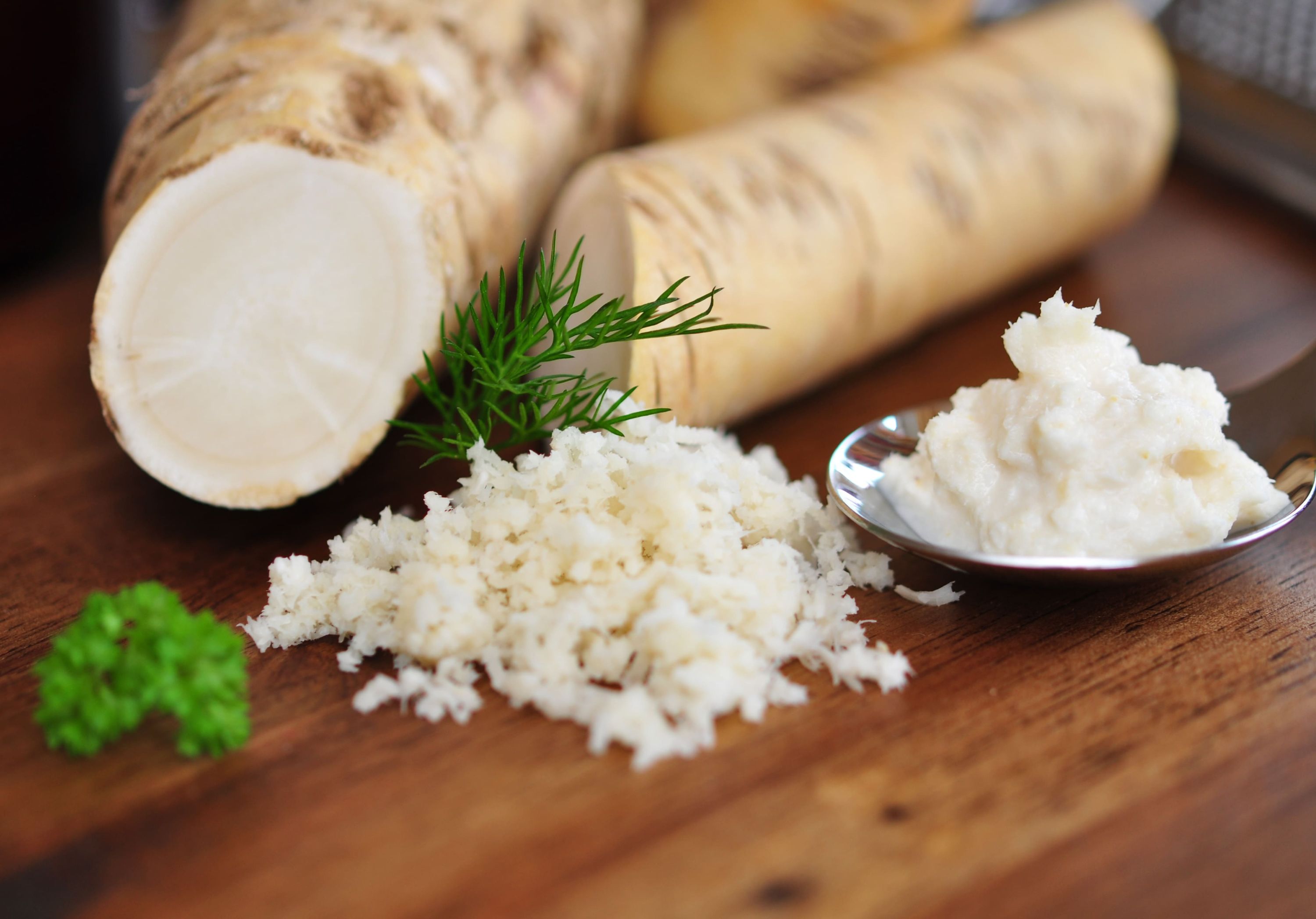 Sections of harvested horseradish root and grated horseradish on a wooden table