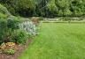 Photo d’une pelouse bien égale et entretenu dans un jardin avec des massifs fleuris.
