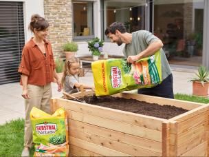 Mutter, Tochter und Vater befüllen ihr Hochbeet mit unserer Substral® Naturen® Hochbeeterde Torffrei.