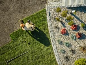 Photo aérienne d’un jardinier qui pose de la terre à gazon dans un jardin bien entretenu avec des bosquets fleuris et une pelouse verte.