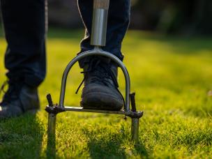 Un jardinier en train d’aérer la pelouse de son jardin avec un outil manuel.