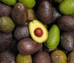 A pile of avocados with one on top cut in half.
