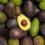 A pile of avocados with one on top cut in half.