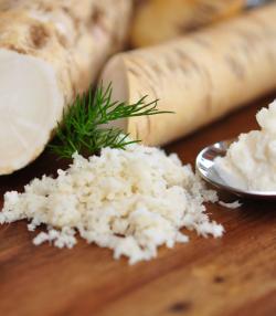Sections of harvested horseradish root and grated horseradish on a wooden table