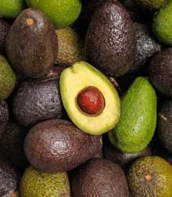 A pile of avocados with one on top cut in half.