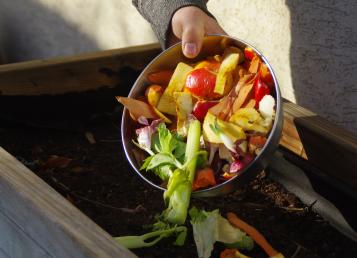 Wooden Compost bin against a grey wall, being filled with food waste 