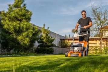 A man mowing a lawn with a lawn mower, showing the difference between overgrown grass and freshly cut grass
