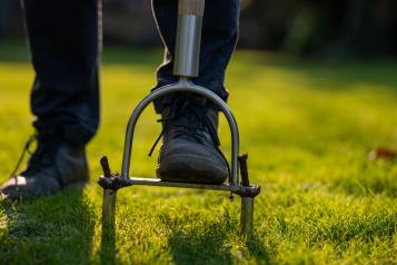 Un jardinier en train d’aérer la pelouse de son jardin avec un outil manuel.