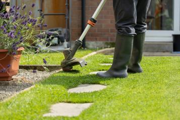 Gardener trimming lawn edge with electric trimmer