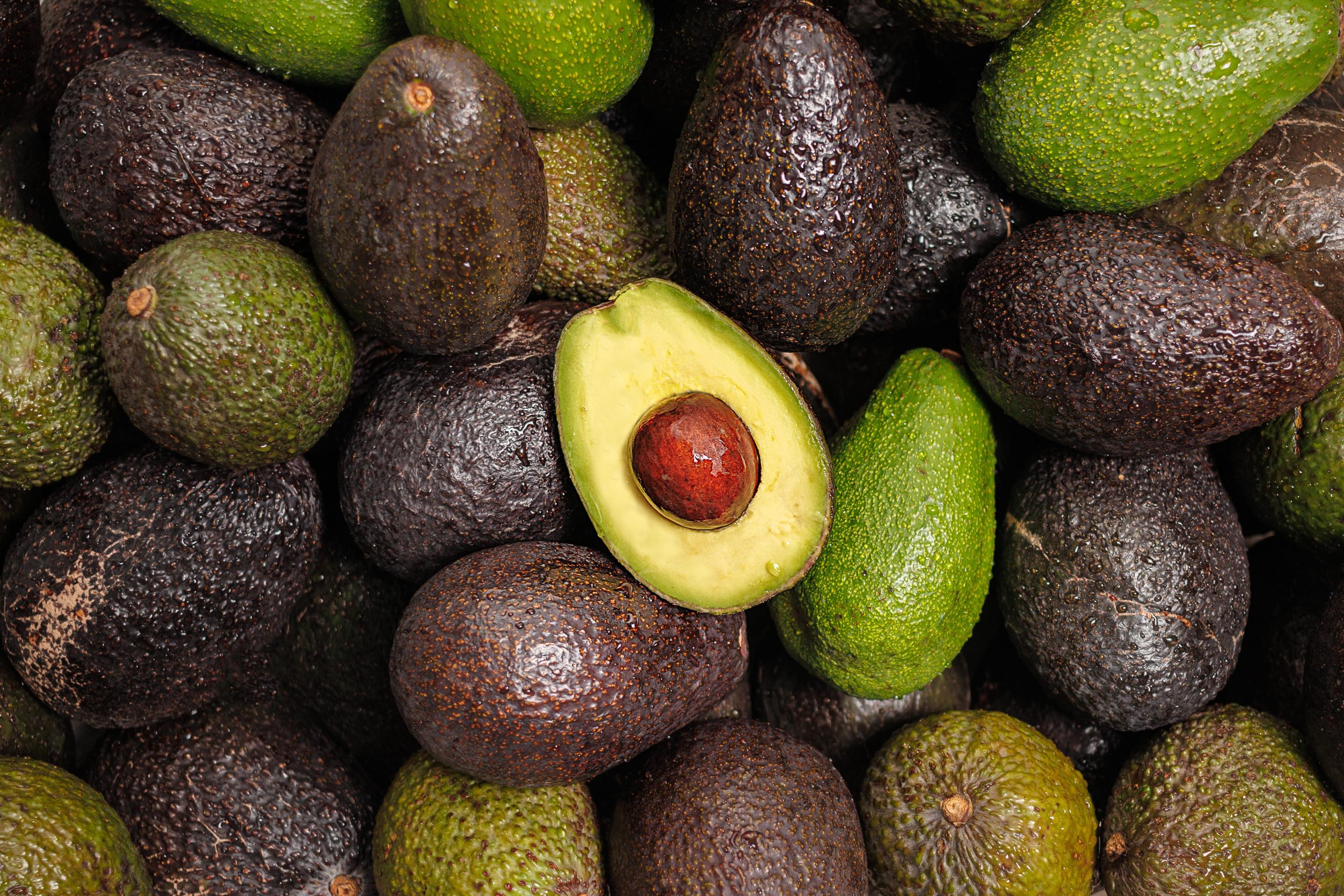 A pile of avocados with one on top cut in half.